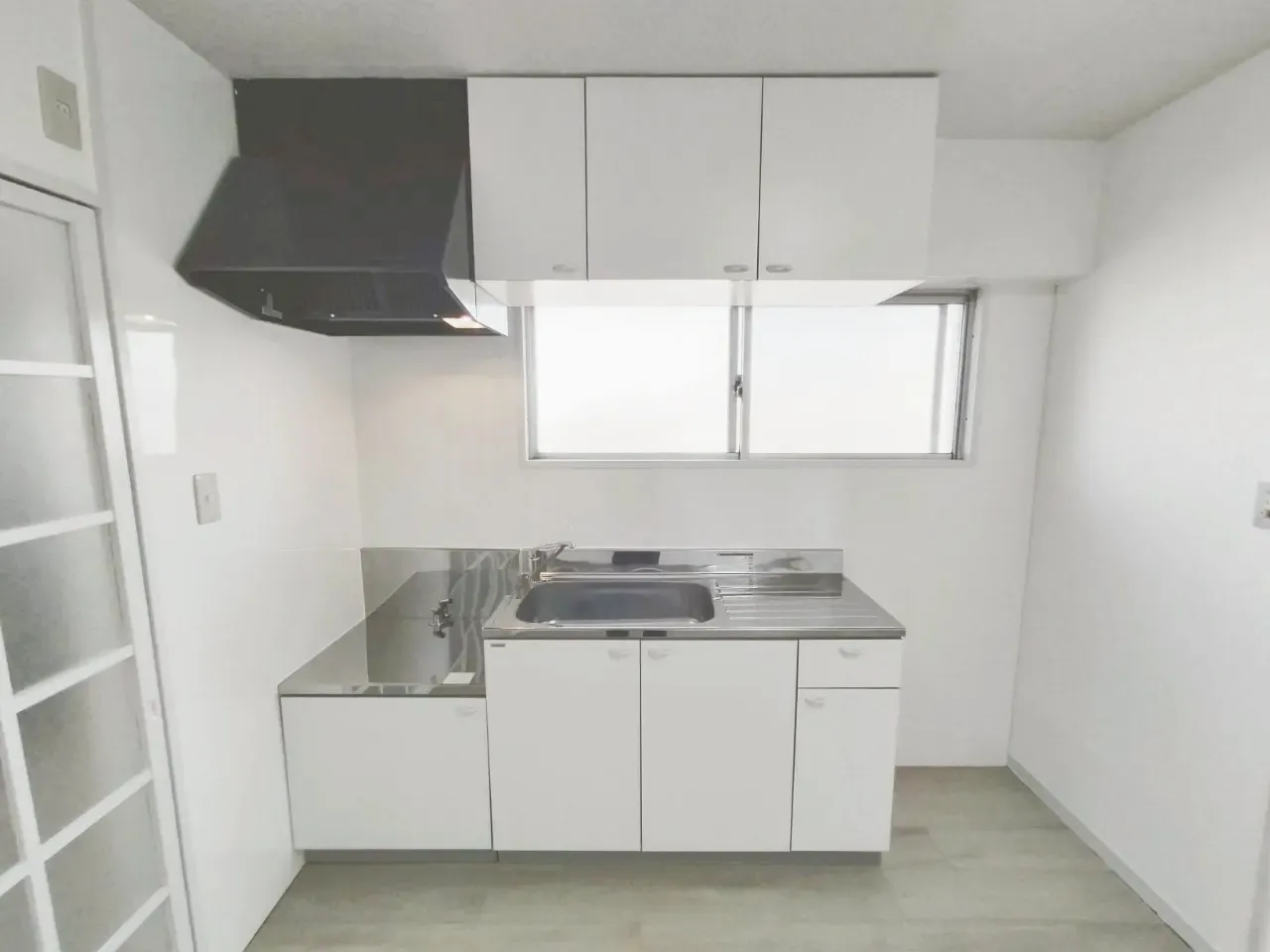 原状回復後の賃貸マンションキッチン。白い収納とステンレス天板の清潔な台所