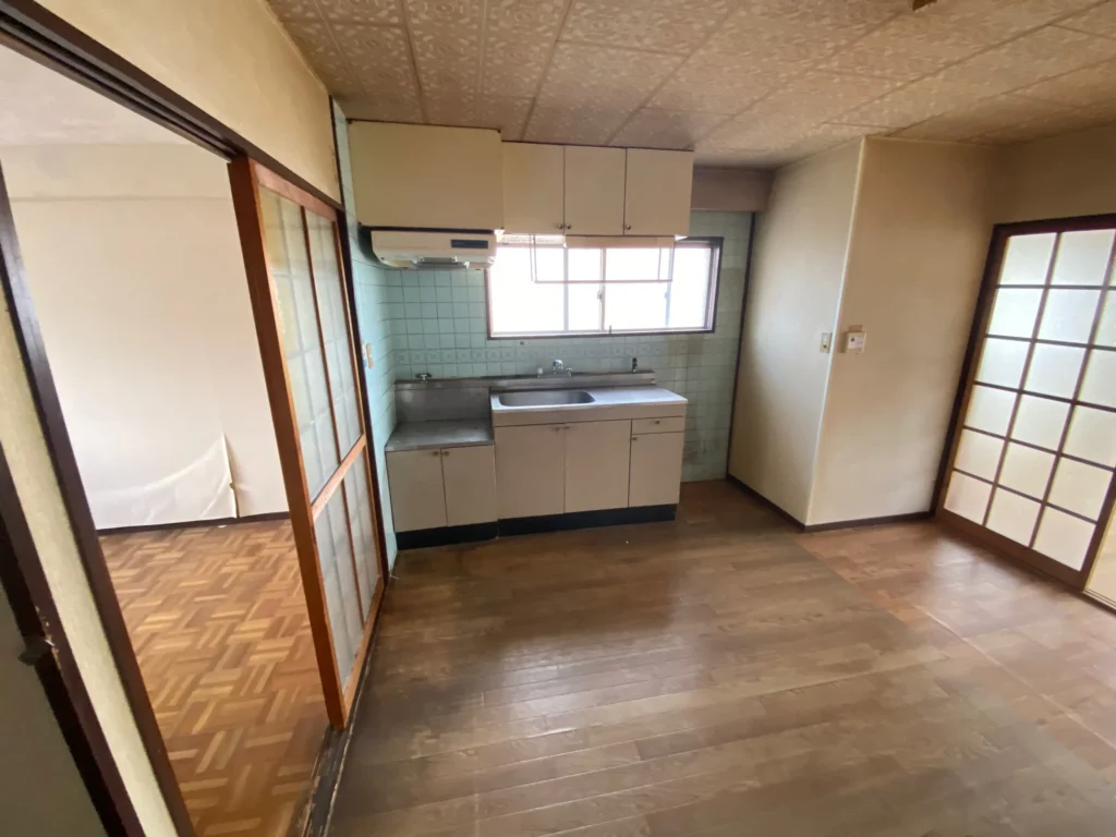 部分改修前の賃貸マンションキッチン。古い流し台と床の状態が分かる室内