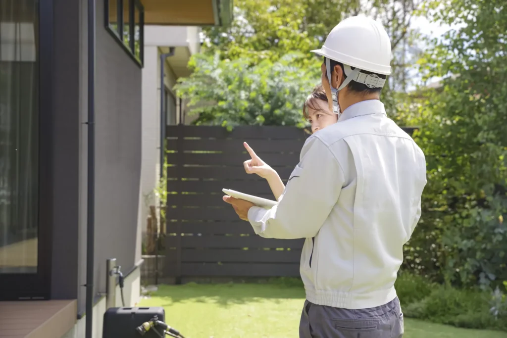 賃貸住宅の改修前現地確認を行うスタッフと入居者。外壁や設備状況をチェックしている様子