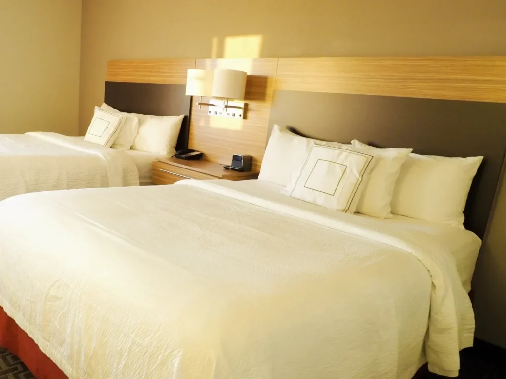 ホテル客室の内装イメージ。ベッドと木目調ヘッドボードの落ち着いた空間