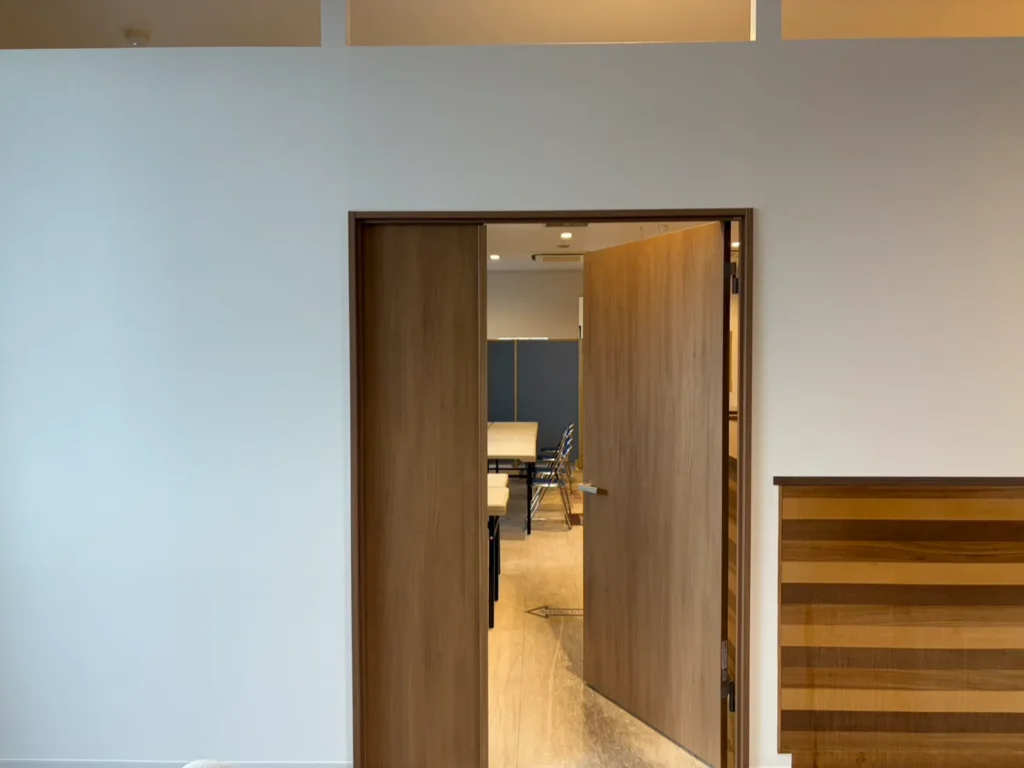 店舗内装リフォーム施工後（After）。白い壁と木目アクセントを組み合わせた新設個室の木製両開きドア周辺の仕上がり