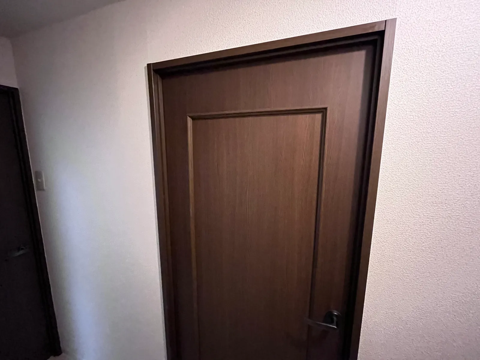 廊下に面した框組デザインの木目調室内ドアと、張り替えた白い壁クロス